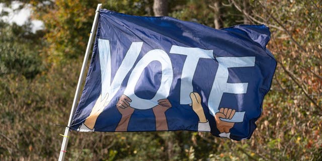 A flag reading VOTE waves as Sen. Raphael Warnock, D-Ga., meets with community members to encourage them to come out and vote on the first day of early voting on Oct. 17, 2022, in Duluth, Georgia. 