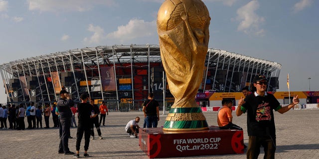 People pose for photos next to a giant replica on the World Cup trophy in front of Stadium 974 on November 18, 2022 in Doha, Qatar, ahead of the Qatar 2022 World Cup football tournament.