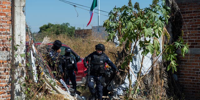 Police officers protect members of the "Hasta Encontrarte" ("Until we find you") collective during the search for missing relatives in a clandestine grave at the Santa Fe neighborhood of Irapuato, Guanajuato state, Mexico, on November 10, 2022.