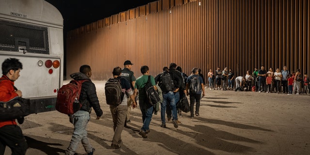 Les immigrants attendent d'être traités par la US Border Patrol après avoir traversé la frontière depuis le Mexique, avec la barrière frontalière américano-mexicaine en arrière-plan, le 6 août 2022 à Yuma, en Arizona. 