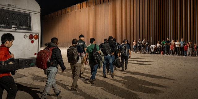 Immigrants wait to be processed by the U.S. Border Patrol after crossing the border from Mexico, with the U.S.-Mexico border barrier in the background, on August 6, 2022 in Yuma, Arizona. 