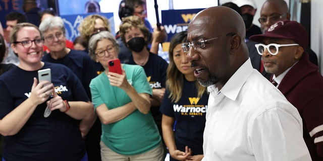 US Sen.  Raphael Warnock, D-Ga., speaks to supporters as film director Spike Lee listens during a canvass launch on November 6, 2022, in Savannah, Georgia. 