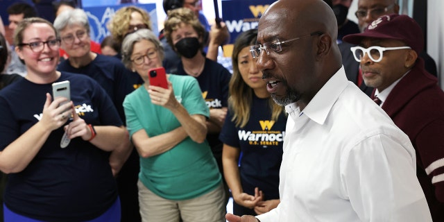 US Sen.  Raphael Warnock, D-Ga., speaks to supporters as film director Spike Lee listens during a canvass launch on November 6, 2022, in Savannah, Georgia. 