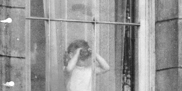Prince Charles using binoculars to view the coronation scene from a window at Buckingham Palace.