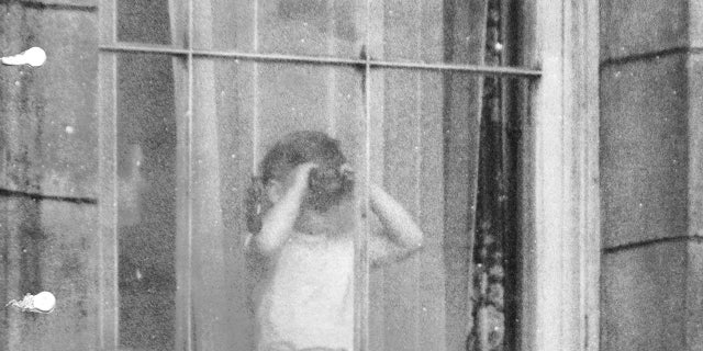 Prince Charles using binoculars to view the coronation scene from a window at Buckingham Palace.