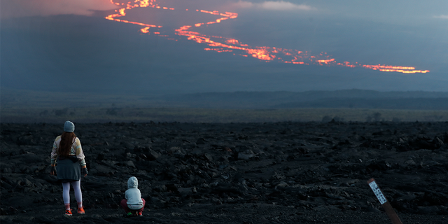 Spectators watch the lava flow down the mountain from the Mauna Loa eruption, Tuesday, Nov. 29, 2022, near Hilo, Hawaii. 