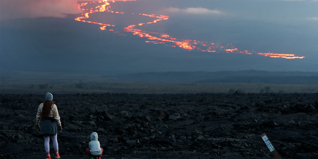 Spectators watch the lava flow down the mountain from the Mauna Loa eruption, Tuesday, Nov. 29, 2022, near Hilo, Hawaii. 