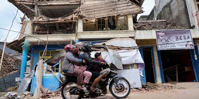 People ride a motorcycle past a building damaged by Monday's earthquake in Cianjur, West Java, Indonesia on Tuesday, Nov. 22, 2022. 