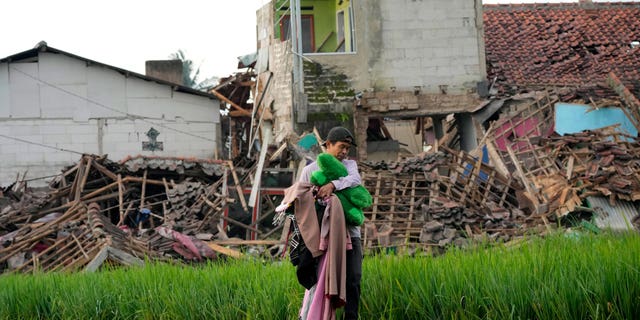 A man carries belongings salvaged from the ruins of his earthquake-damaged house in Cianjur, West Java, Indonesia Tuesday, Nov. 22, 2022. 