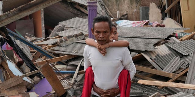 A man carries his son past ruins of houses damaged in Monday's earthquake in Cianjur, West Java, Indonesia Tuesday, Nov. 22, 2022. 
