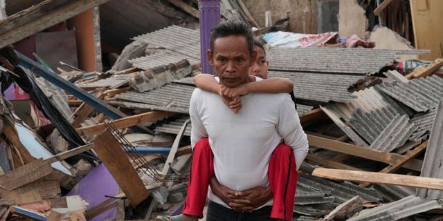 A man carries his son past ruins of houses damaged in Monday's earthquake in Cianjur, West Java, Indonesia Tuesday, Nov. 22, 2022. 