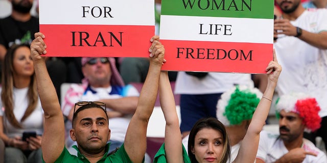 イランのサッカーファンは、2022年11月21日月曜日、カタールのドーハにあるハリファ国際スタジアムで、イングランドとイランの間のワールドカップグループBサッカーの試合の前に、Woman Life FreedomとFreedom For Iranと書かれた看板を掲げています.