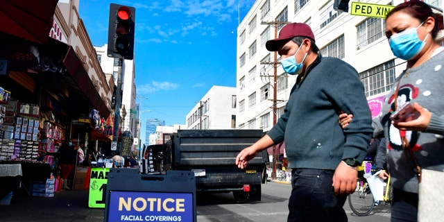 A sign reminds people of the requirement to wear face coverings while pedestrians wear face masks due to the coronavirus in Los Angeles, California on November 12, 2020. 