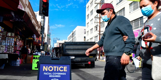 A signboard reminds people of the face covering requirement as pedestrians wear facemasks due to the coronavirus in Los Angeles, California on November 12, 2020. - European and world leaders on November 12, 2020 insisted that when Covid-19 vaccines are launched they should be made a available to everyone, under an international project which still needs $28 billion of funding. (Photo by Frederic J. BROWN / AFP) 