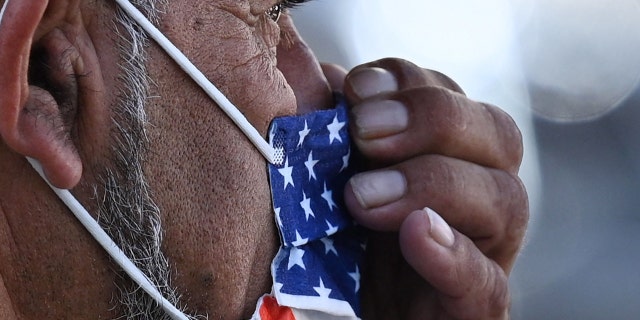 A man adjusts his American flag face mask on July 19, 2021, on a street in Hollywood, California, on the second day of the return of the indoor mask mandate in Los Angeles County due to a spike in coronavirus cases.
