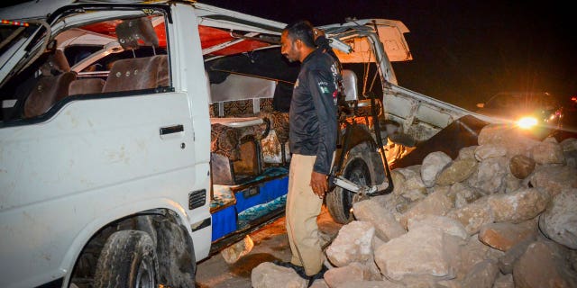 A policeman stands beside a damaged passenger mini bus after an overnight accident in Sehwan of Sindh province, on Nov. 18, 2022.