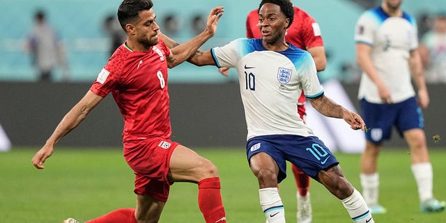 Iran's Morteza Pouraliganji, left, is challenged by England's Raheem Sterling during the World Cup group B soccer match between England and Iran at the Khalifa International Stadium, in Doha, Qatar, Monday, Nov. 21, 2022. 