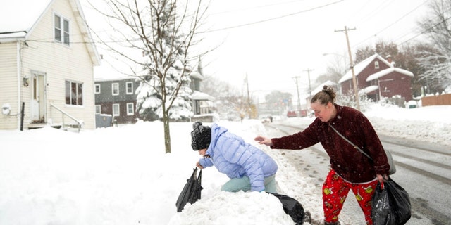 Rachel Grigsby tries to steady her daughter Mia Grigsby, 9, as she climbs over a snowbank, heading home from a trip to the corner store in Buffalo, N.Y., Friday, Nov. 18, 2022.