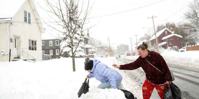 Rachel Grigsby tries to steady her daughter Mia Grigsby, 9, as she climbs over a snowbank, heading home from a trip to the corner store in Buffalo, N.Y., Friday, Nov. 18, 2022.