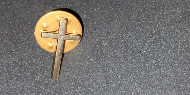 Timms porte la croix non seulement comme symbole de sa foi chrétienne, mais aussi en mémoire de sa défunte épouse.