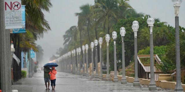 A pair of beach goers walk on the Hollywood Beach boardwalk as conditions deteriorate with the approach of Hurricane Nicole, Wednesday, Nov. 9, 2022, in Hollywood Beach in Hollywood, Fla.