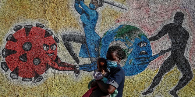 Une femme et un enfant passent devant une peinture murale informative illustrant la bataille mondiale contre le coronavirus dans une rue de Kericho, au Kenya, le 26 janvier 2022.