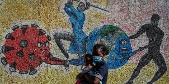 Une femme et un enfant passent devant une peinture murale informative illustrant la bataille mondiale contre le coronavirus dans une rue de Kericho, au Kenya, le 26 janvier 2022.