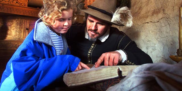 Pilgrim Edward Winslow, portrayed by Michael Hall, reads a passage from the Bible with Leah Pearl, 8, of Nantucket, as she visited his home at the Plimoth Plantation in Plymouth, Massachusetts. 