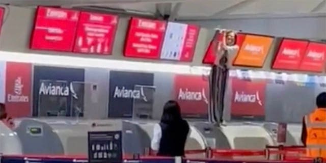 Інші пасажири в аеропорту можуть здалеку побачити неконтрольовану особу, яка стоїть біля стійки реєстрації та тримає над нею екран.