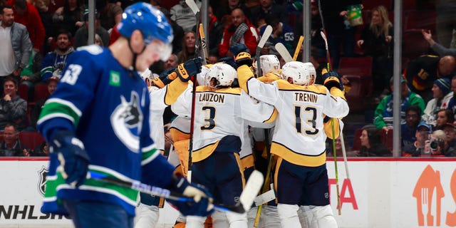 Bo Horvat of the Vancouver Canucks, foreground, passes as Nashville Predators players celebrate a victory at Rogers Arena on November 5, 2022 in Vancouver, British Columbia, Canada.