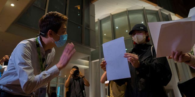 A University staffer checks the identity of protesters during a protest gathering at the University of Hong Kong in Hong Kong, Tuesday, Nov. 29, 2022. On Tuesday, about a dozen people gathered at the University of Hong Kong, chanting against virus restrictions and holding up sheets of paper with critical slogans. Most were from the mainland, which has a separate legal system from the Chinese territory of Hong Kong, and some spectators joined in their chants.