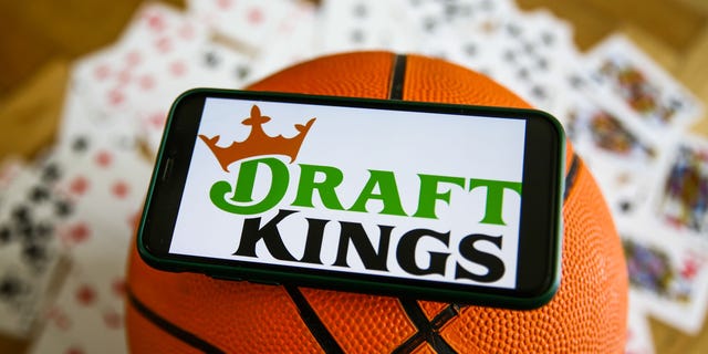 The DraftKings logo displayed on a mobile phone, a basketball and playing cards are seen in this illustrative photo taken on September 21, 2021 in Krakow, Poland.