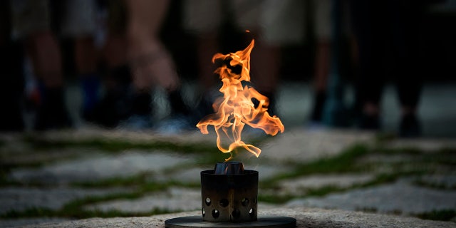 People can be seen in the background visiting the Eternal Flame at the grave of former President John F. Kennedy near the 100th anniversary of his birth at Arlington National Cemetery on May 26, 2017, in Arlington, Virginia.