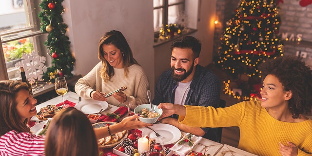 Teman bersenang-senang merayakan Natal, duduk di meja, makan, minum anggur dan bersenang-senang sambil menghabiskan waktu bersama selama liburan musim dingin