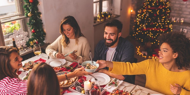 Friends having fun celebrating Christmas, sitting at the table, eating, drinking wine and having fun while spending time together during winter holidays