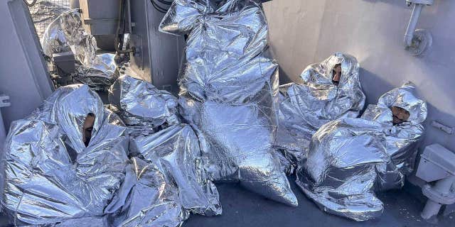 Migrants saved by Greek coast guards wear thermal blankets to keep warm while on a ship in the Aegean Sea, Greece, on Tuesday, Nov. 1, 2022.