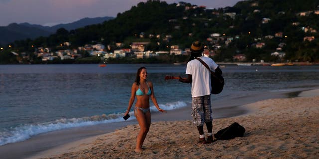 A woman is serenaded by a man playing the guitar and singing Bob Marley music at Grand Anse Beach during sunset in St. George's, Grenada