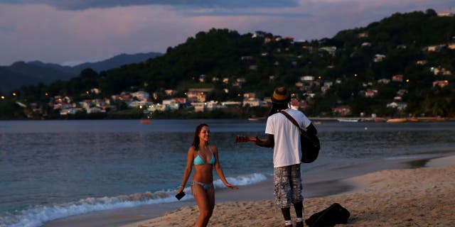 A woman is serenaded by a man playing the guitar and singing Bob Marley music at Grand Anse Beach during sunset in St. George's, Grenada