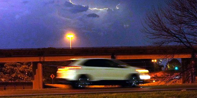 A vehicle races along a Jackson, Miss., street as lightning streaks across the sky.