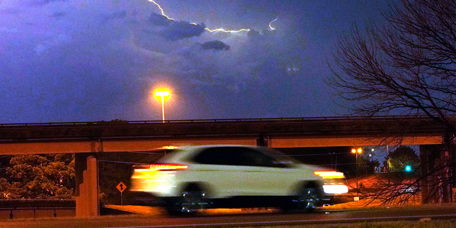 A vehicle races along a street in Jackson, Mississippi as lightning bolts cross the sky.