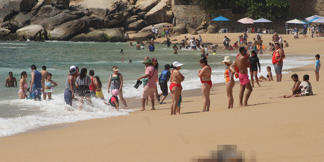 Des touristes sur la plage près de l'un des trois corps portant des signes de torture qui se sont échoués, selon les médias locaux, à Acapulco, au Mexique, le 12 novembre 2022.