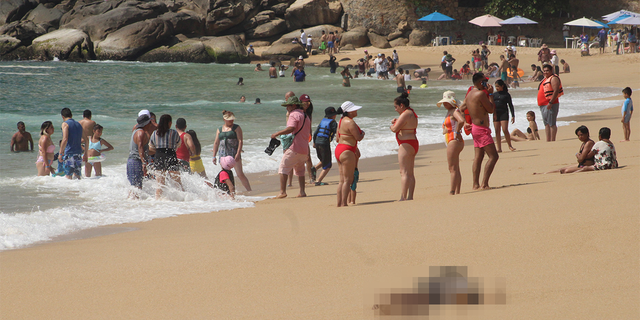 Tourists enjoy the beach near one of three bodies with signs of torture that were washed ashore by the sea, according to local media, at Icacos beach, in Acapulco, Mexico Nov. 12, 2022. 