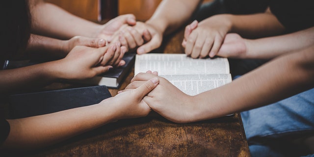 people holding hands in prayer around Bible
