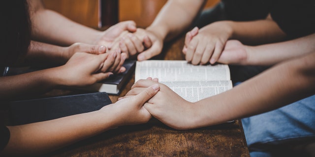 people holding hands in prayer around Bible