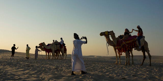 A tour guide takes a photo of a couple atop camels in Mesaieed, Qatar, Nov. 26, 2022. Throngs of World Cup fans in Qatar looking for something to do between games are leaving Doha for a classic Gulf tourist experience: riding a camel in the desert. But the sudden rise in tourists is putting pressure on the animals, who have almost no time to rest between each ride.