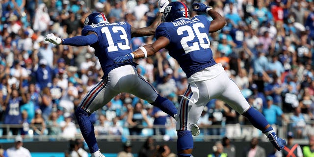 Ses coéquipiers Odell Beckham Jr. (13) et Saquon Barkley (26) des Giants de New York célèbrent après que Beckham Jr. ait lancé un touché à Barkley lors d'un match au stade Bank of America le 7 octobre 2018 à Charlotte, en Caroline du Nord 