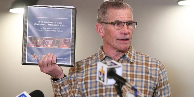 Former Oxford Community Schools Board President Tom Donnelly presents a binder labelled "Enhancing School Safety Using a Threat Assessment Model, an operational guide for preventing targeted school violence" at a Monday press conference. Donnelly was one of multiple school officials to note that guidelines the publication listed were not properly followed in the leadup to the 2021 Oxford High School shooting.