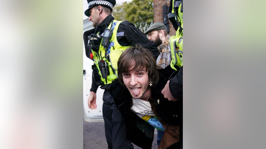 Protestor sticks out his tongue after being detained by police for hurling egg at King Charles