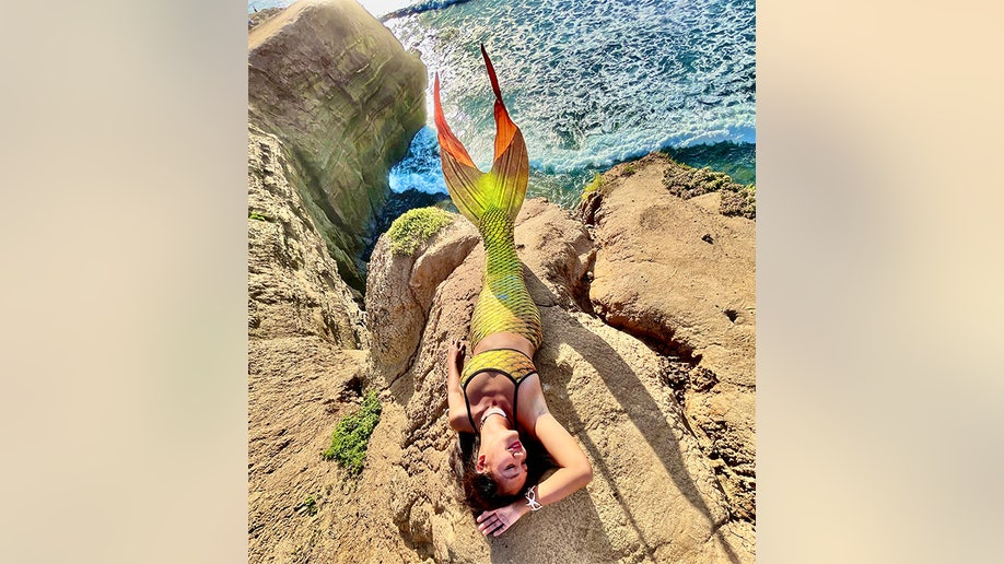 Great Chin Burger poses cliffside in a yellow mermaid tail and a matching fish scale top