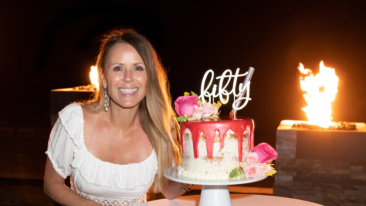 Trista Sutter with a white dress on celebrates her 50th birthday with a white and pink cake